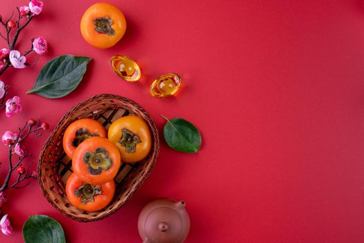 Top view of fresh sweet persimmons kaki with leaves on red table background for Chinese lunar new year fruit design concept, the word means spring is coming.