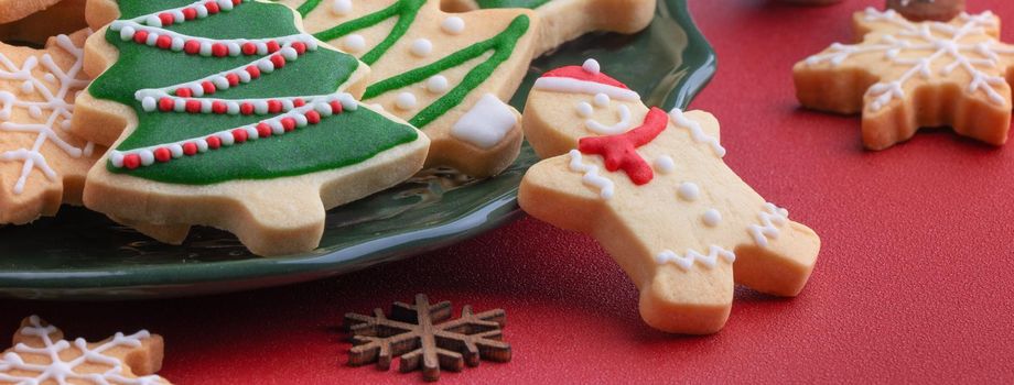 Close up of Christmas decorated sugar cookies in a plate on red table background.