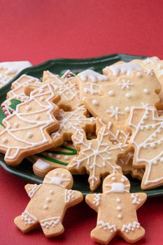 Close up of Christmas decorated sugar cookies in a plate on red table background.