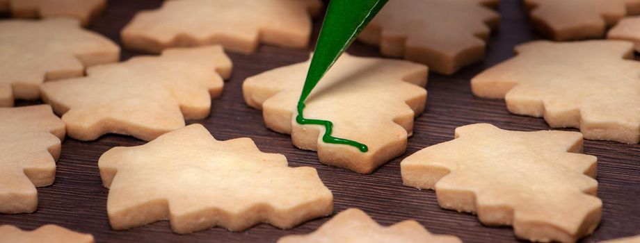 Close up of drawing gingerbread Christmas tree sugar cookie on wooden table background with green icing, concept of holiday celebration.