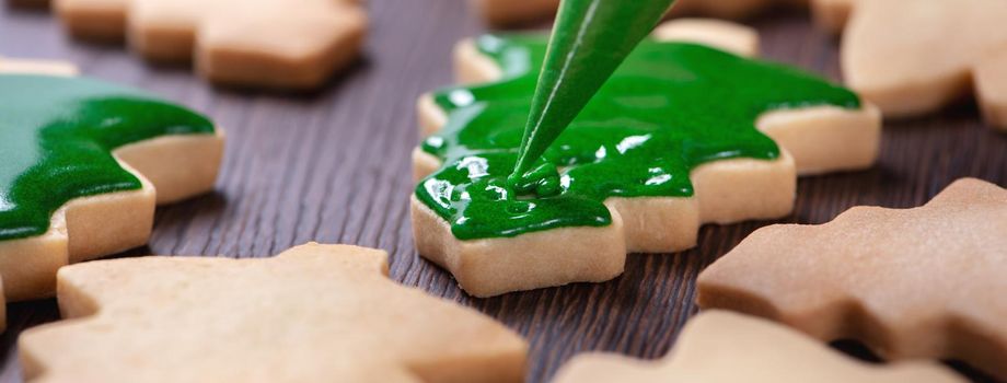 Close up of drawing gingerbread Christmas tree sugar cookie on wooden table background with green icing, concept of holiday celebration.