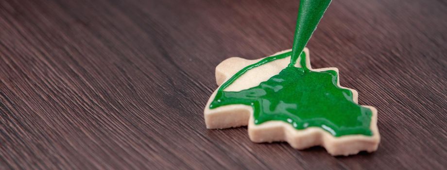 Close up of drawing gingerbread Christmas tree sugar cookie on wooden table background with green icing, concept of holiday celebration.
