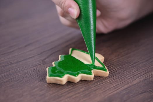 Close up of drawing gingerbread Christmas tree sugar cookie on wooden table background with green icing, concept of holiday celebration.