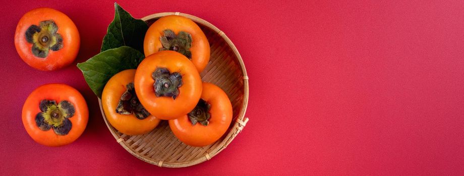 Top view of fresh sweet persimmons kaki with leaves on red table background for Chinese lunar new year fruit design concept, the word means spring is coming.