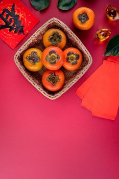 Top view of fresh sweet persimmons kaki with leaves on red table background for Chinese lunar new year fruit design concept, the word means spring is coming.