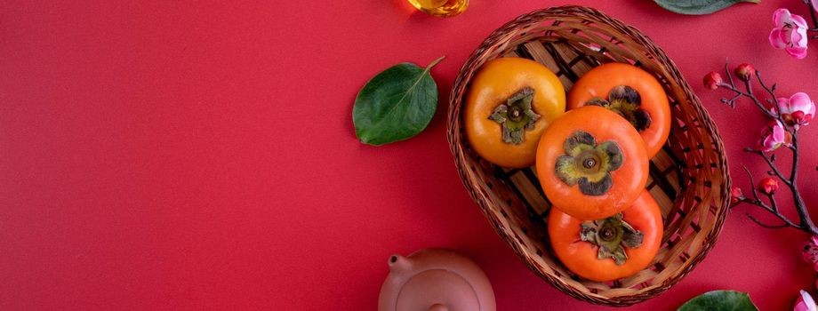 Top view of fresh sweet persimmons kaki with leaves on red table background for Chinese lunar new year fruit design concept, the word means spring is coming.