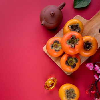 Top view of fresh sweet persimmons kaki with leaves on red table background for Chinese lunar new year fruit design concept, the word means spring is coming.