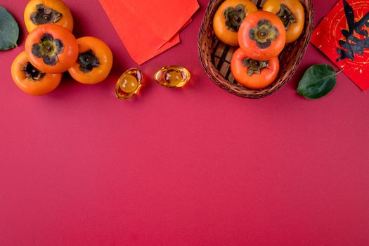 Top view of fresh sweet persimmons kaki with leaves on red table background for Chinese lunar new year fruit design concept, the word means spring is coming.