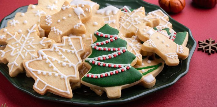 Close up of Christmas decorated sugar cooikes in a plate on red table background.