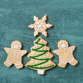 Top view of Christmas tree and snowflake cooikes with gingerbread man wearing mask on green table background.