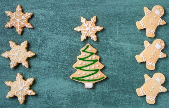 Top view of Christmas tree and snowflake cooikes with gingerbread man wearing mask on green table background.