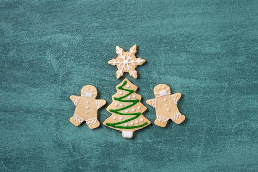 Top view of Christmas tree and snowflake cooikes with gingerbread man wearing mask on green table background.