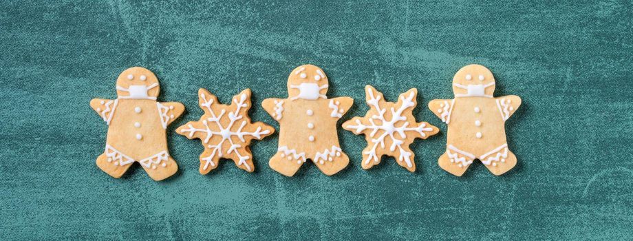 Top view of Christmas tree and snowflake cooikes with gingerbread man wearing mask on green table background.