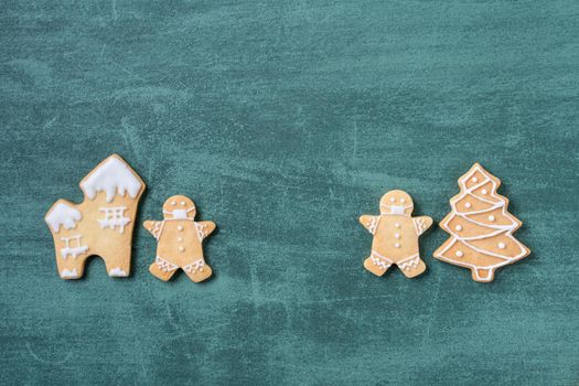 Top view of Christmas tree and snowflake cooikes with gingerbread man wearing mask on green table background.