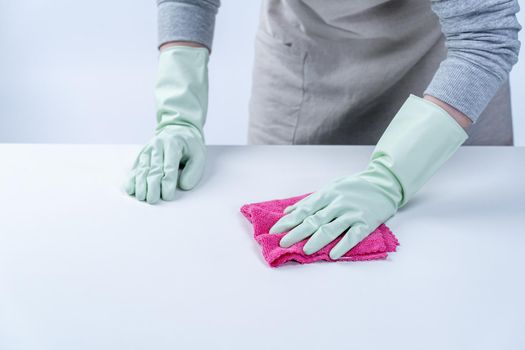 Young woman housekeeper in apron is cleaning, wiping down table surface with wet rag, spraying bottle cleaner to prevent disease spreading.