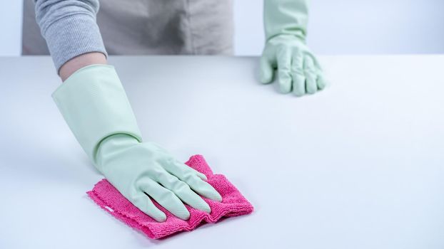 Young woman housekeeper in apron is cleaning, wiping down table surface with wet rag, spraying bottle cleaner to prevent disease spreading.