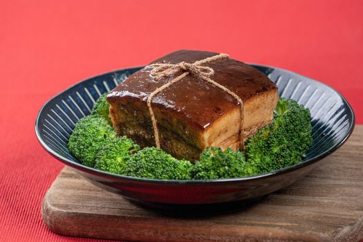 Dong Po Rou (Dongpo pork meat) in a beautiful blue plate with green broccoli vegetable, traditional festive food for Chinese new year cuisine meal, close up.