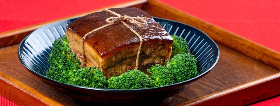 Dong Po Rou (Dongpo pork meat) in a beautiful blue plate with green broccoli vegetable, traditional festive food for Chinese new year cuisine meal, close up.