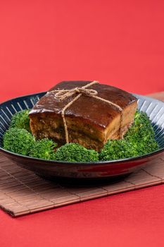 Dong Po Rou (Dongpo pork meat) in a beautiful blue plate with green broccoli vegetable, traditional festive food for Chinese new year cuisine meal, close up.