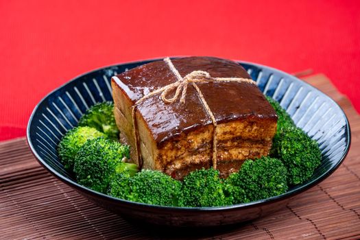 Dong Po Rou (Dongpo pork meat) in a beautiful blue plate with green broccoli vegetable, traditional festive food for Chinese new year cuisine meal, close up.