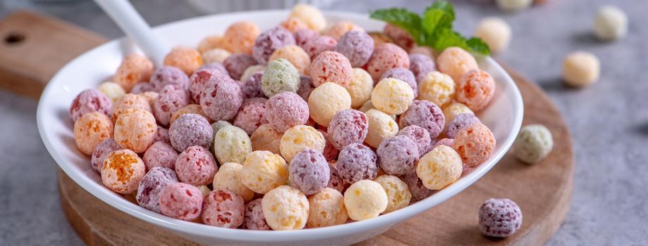 Colorful cereal corn balls mix, fruit flavor bowl sweets on gray cement background, close up, fresh, delicious and healthy breakfast, copy space design concept.