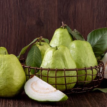 Close up of delicious beautiful guava set with fresh green leaves isolated on dark wooden table background.