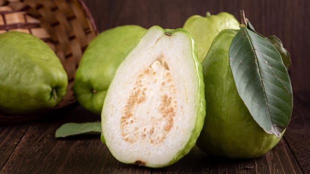 Close up of delicious beautiful guava set with fresh green leaves isolated on dark wooden table background.