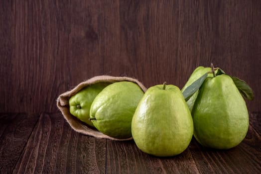 Close up of delicious beautiful guava set with fresh green leaves isolated on dark wooden table background.