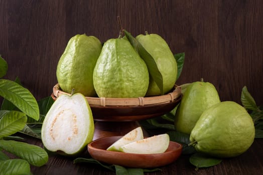 Close up of delicious beautiful guava set with fresh green leaves isolated on dark wooden table background.