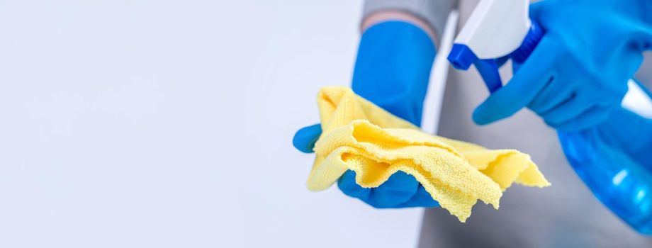 Young woman housekeeper in apron is cleaning, wiping down table surface with wet rag, spraying bottle cleaner to prevent disease spreading.