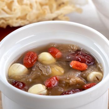 Close up of traditional Chinese sweet snow white fungus soup with lotus seed, red dates (jujube) and wolfberry (goji, gojiberry) on white background.