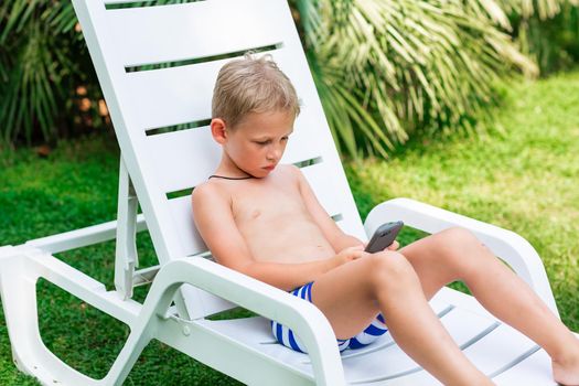 Boy playing games on the telephone. Gadget dependency disorder problem for kids during holiday vacation at the seaside concept