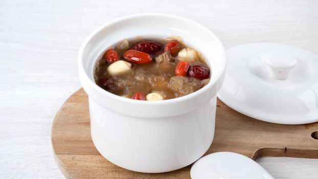 Close up of traditional Chinese sweet snow white fungus soup with lotus seed, red dates (jujube) and wolfberry (goji, gojiberry) on white background.