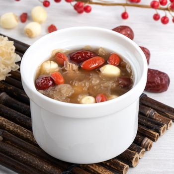 Close up of traditional Chinese sweet snow white fungus soup with lotus seed, red dates (jujube) and wolfberry (goji, gojiberry) on white background.