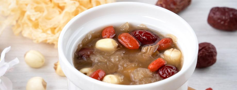 Close up of traditional Chinese sweet snow white fungus soup with lotus seed, red dates (jujube) and wolfberry (goji, gojiberry) on white background.