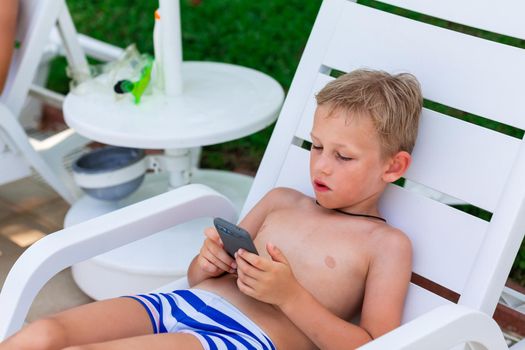 Boy playing games on the telephone. Gadget dependency disorder problem for kids during holiday vacation at the seaside concept