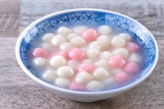 Close up of red and white tangyuan (tang yuan, glutinous rice dumpling balls) in blue bowl on wooden background for Winter solstice festival food.