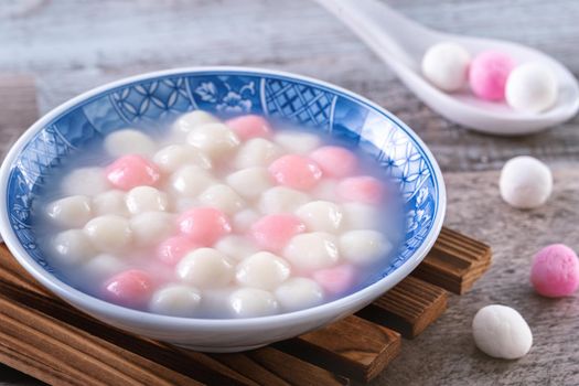 Close up of red and white tangyuan (tang yuan, glutinous rice dumpling balls) in blue bowl on wooden background for Winter solstice festival food.