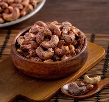 Cashew nuts with peel in a wooden bowl on wooden tray and table background, healthy raw food plate.