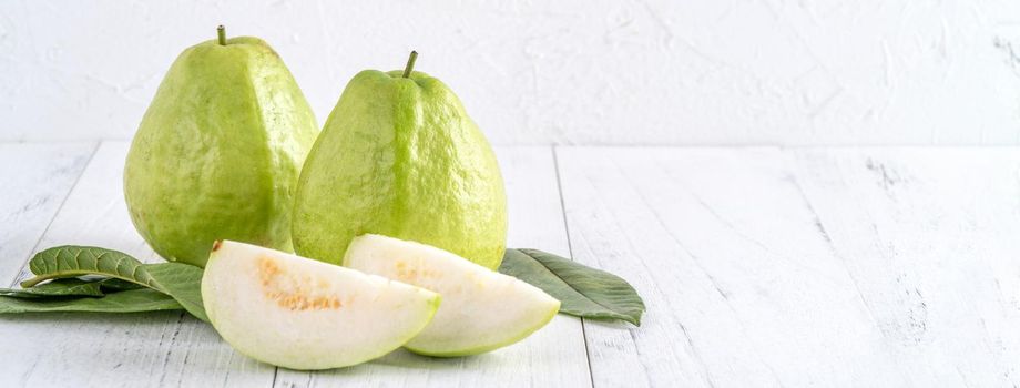 Delicious beautiful guava set with fresh leaves isolated on bright white wooden table background, close up.