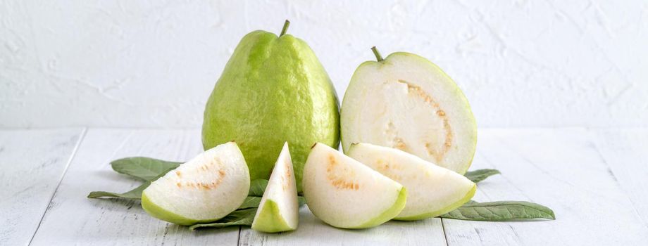 Delicious beautiful guava set with fresh leaves isolated on bright white wooden table background, close up.