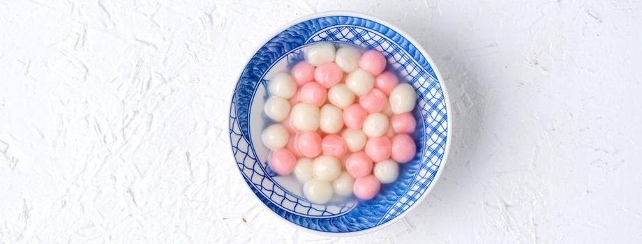 Top view of red and white tangyuan (tang yuan, glutinous rice dumpling balls) in blue bowl on white background for Winter solstice festival food.