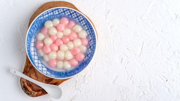 Top view of red and white tangyuan (tang yuan, glutinous rice dumpling balls) in blue bowl on white background for Winter solstice festival food.