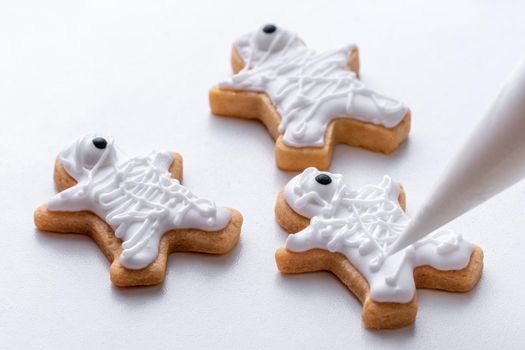 Close up of decorating cute Halloween gingerbread cookies with frosting icing cream topping bag.
