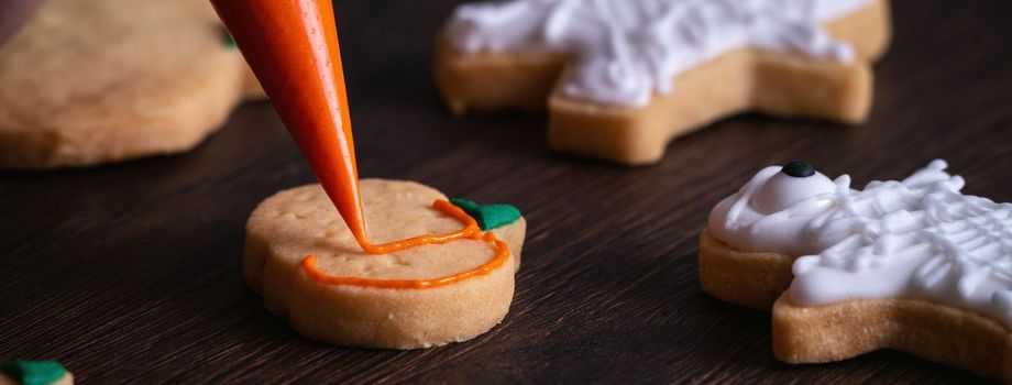 Close up of decorating cute Halloween pumpkin gingerbread cookies with frosting icing cream topping bag.