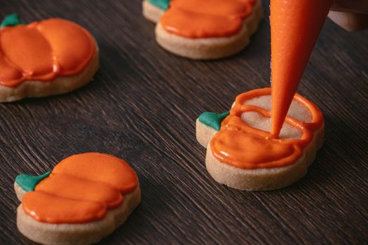 Close up of decorating cute Halloween pumpkin gingerbread cookies with frosting icing cream topping bag.