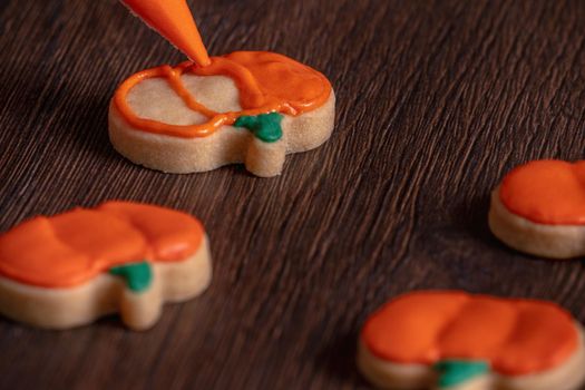 Close up of decorating cute Halloween pumpkin gingerbread cookies with frosting icing cream topping bag.