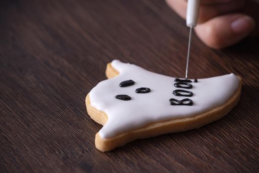 Close up of decorating cute Halloween ghost gingerbread cookies with frosting icing cream topping bag.