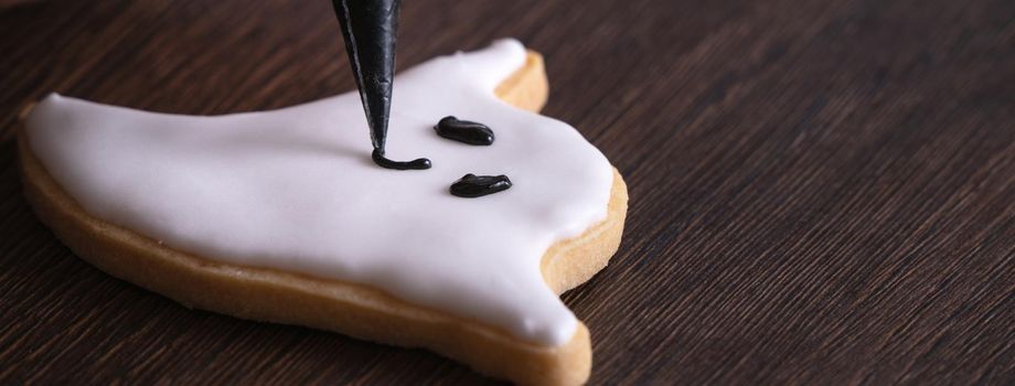 Close up of decorating cute Halloween ghost gingerbread cookies with frosting icing cream topping bag.