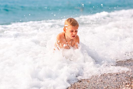 Happy active little boy having fun in the spalshes in the waves at the seaside